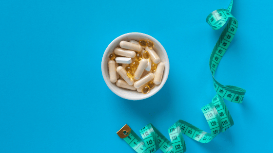 A green measuring tape and weight loss pills in a white bowl